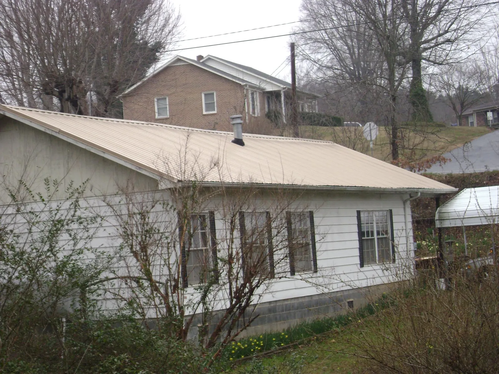 Tan metal roof on a white sided house set into a hillside — Commercial Roofing by Roofing Brothers in Ridgefield